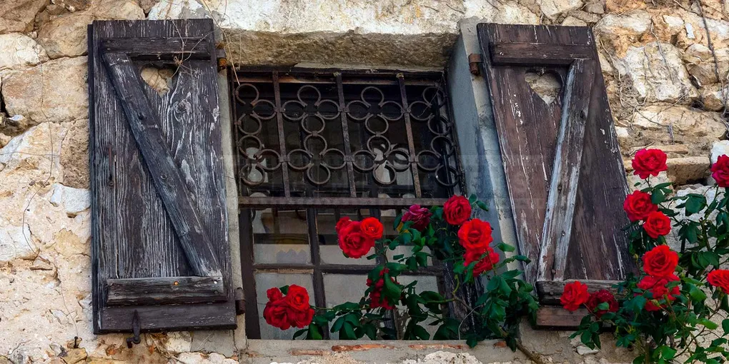 Beautiful medieval window with red roses in Eze Village