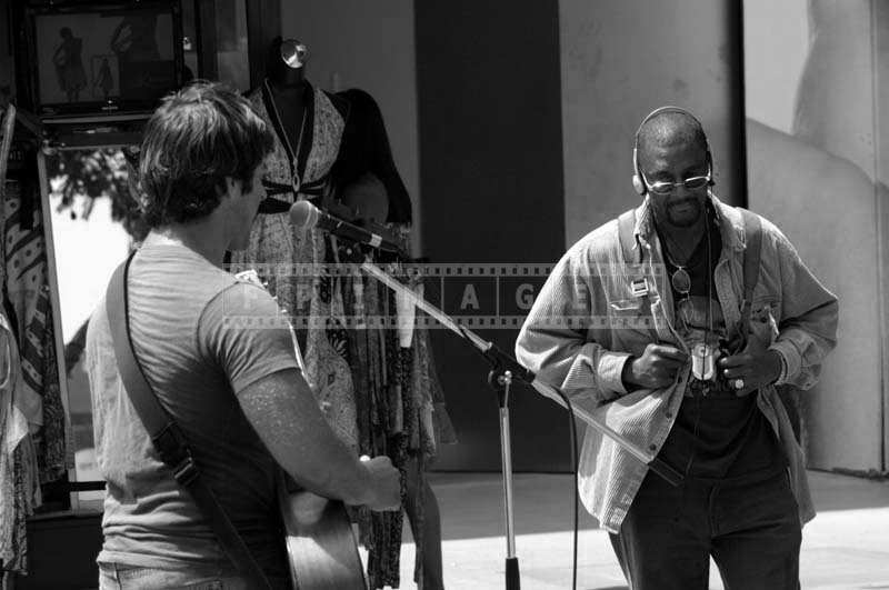 Man Wearing Headphones Walks on as a Street Musician Performs