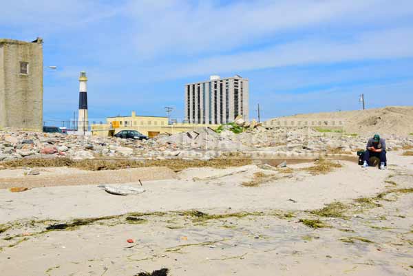 Absecon lighthouse and a man sitting on the shore littered with broken pieces of buildings