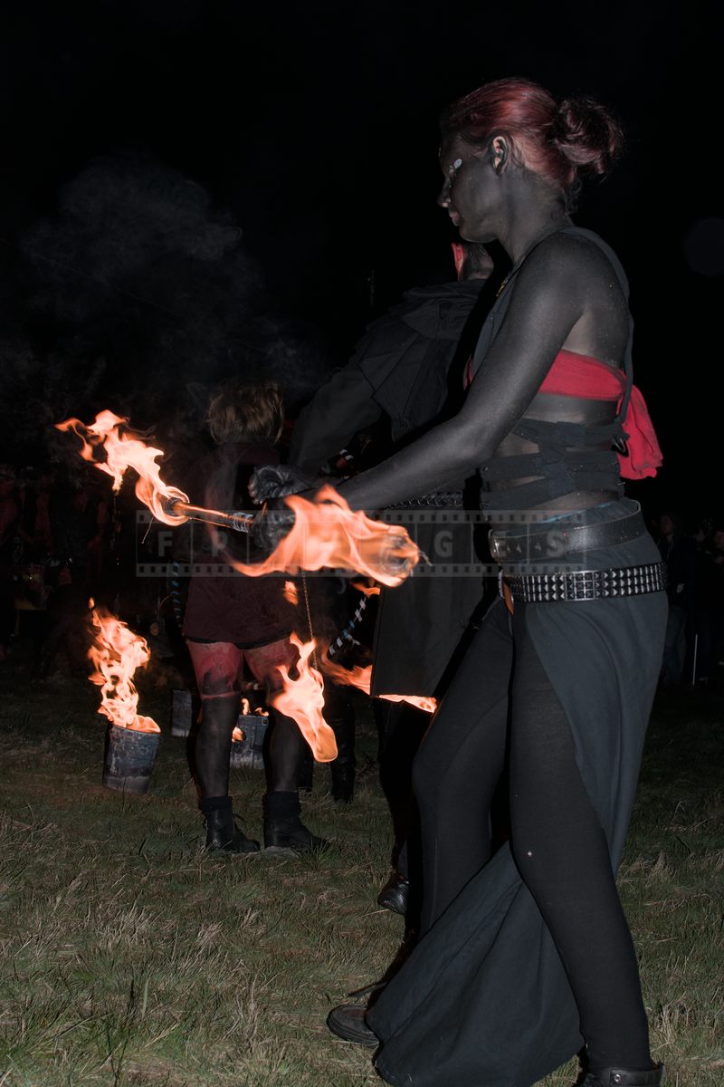 Skin painted black artist twirls fire staff